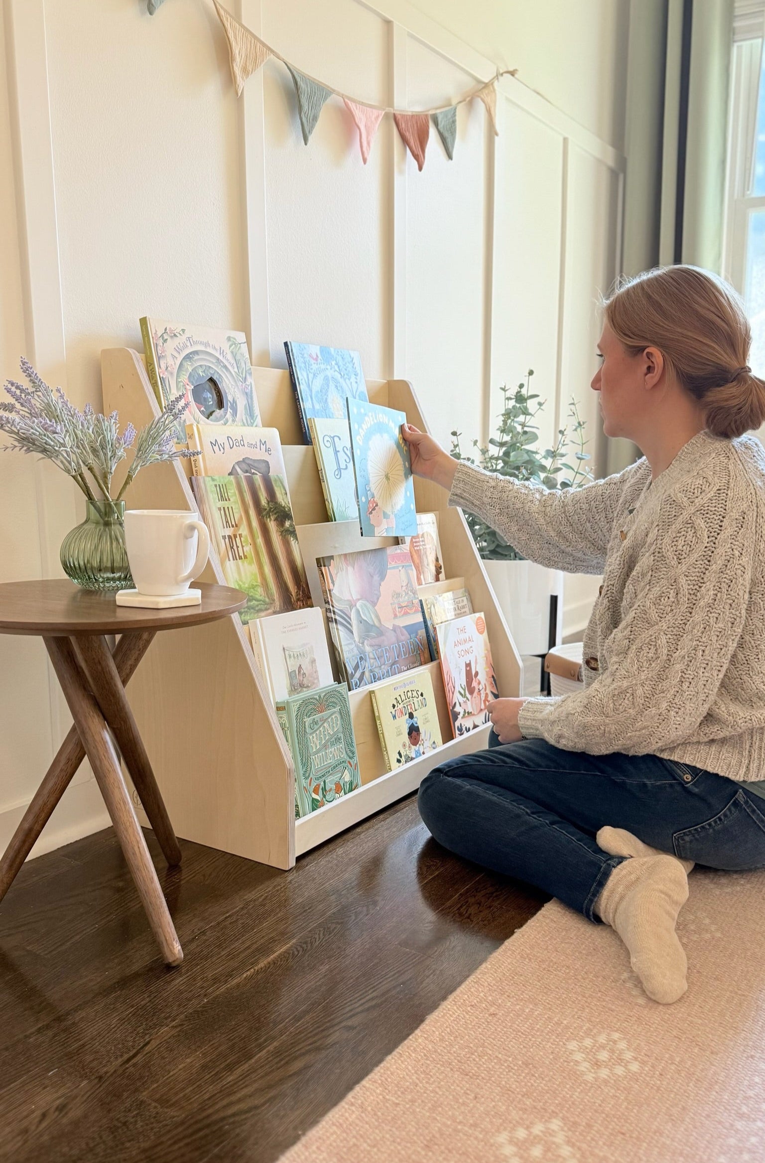 Woman arranging books on a wooden bookshelf in a cozy room.