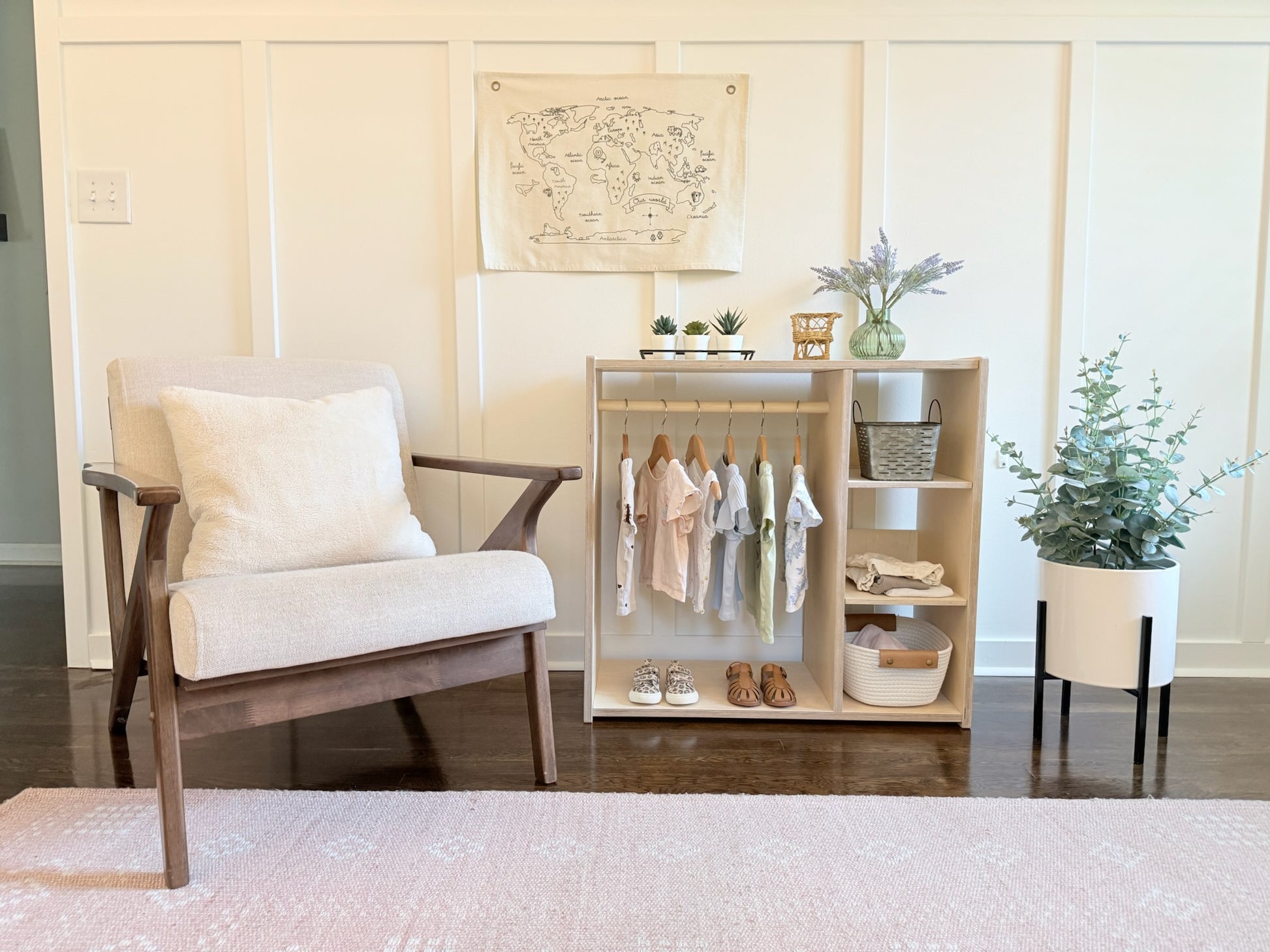 Modern interior with a white armchair, wooden shelf with clothes, and plants.