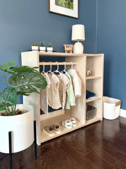 Children's Montessori style wardrobe with hanging and folded clothes and storage against a blue corner wall.