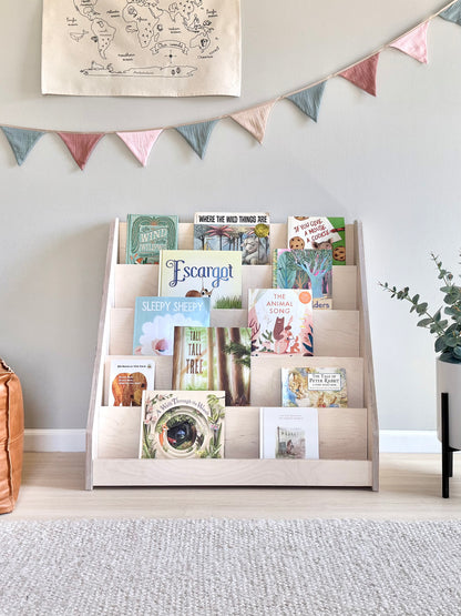 Children's bookshelf with a variety of books displayed on the shelves, positioned in a room with decorative flags hanging on the wall.