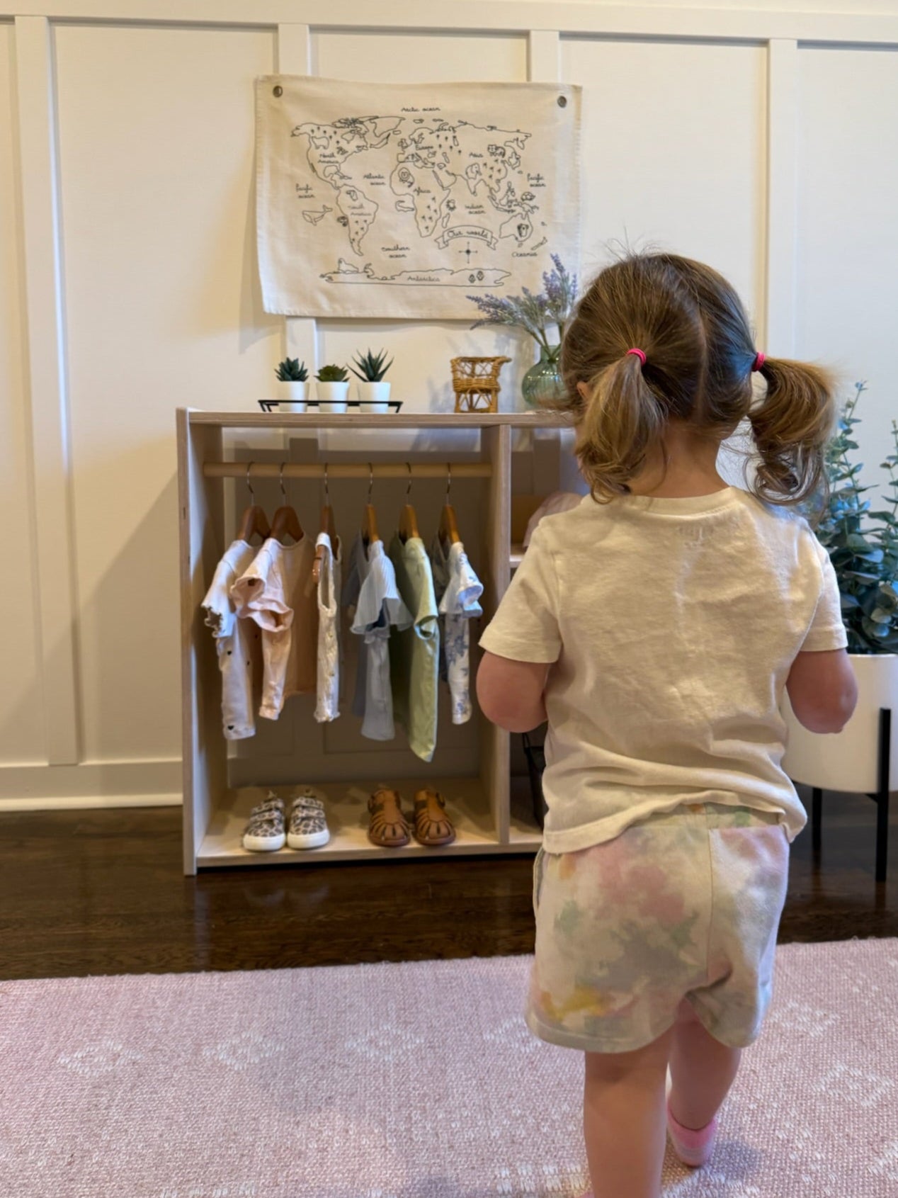 Child looking at a display of children's clothes in a room with a map on the wall.