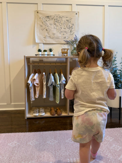 Child looking at a display of children's clothes in a room with a map on the wall.
