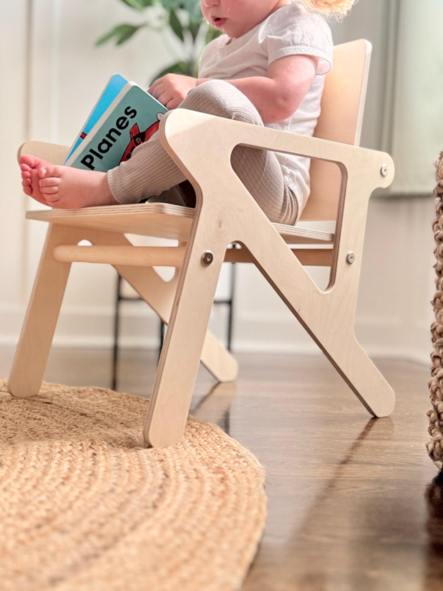 Child sitting in a wooden mid-century modern style chair holding a book indoors.