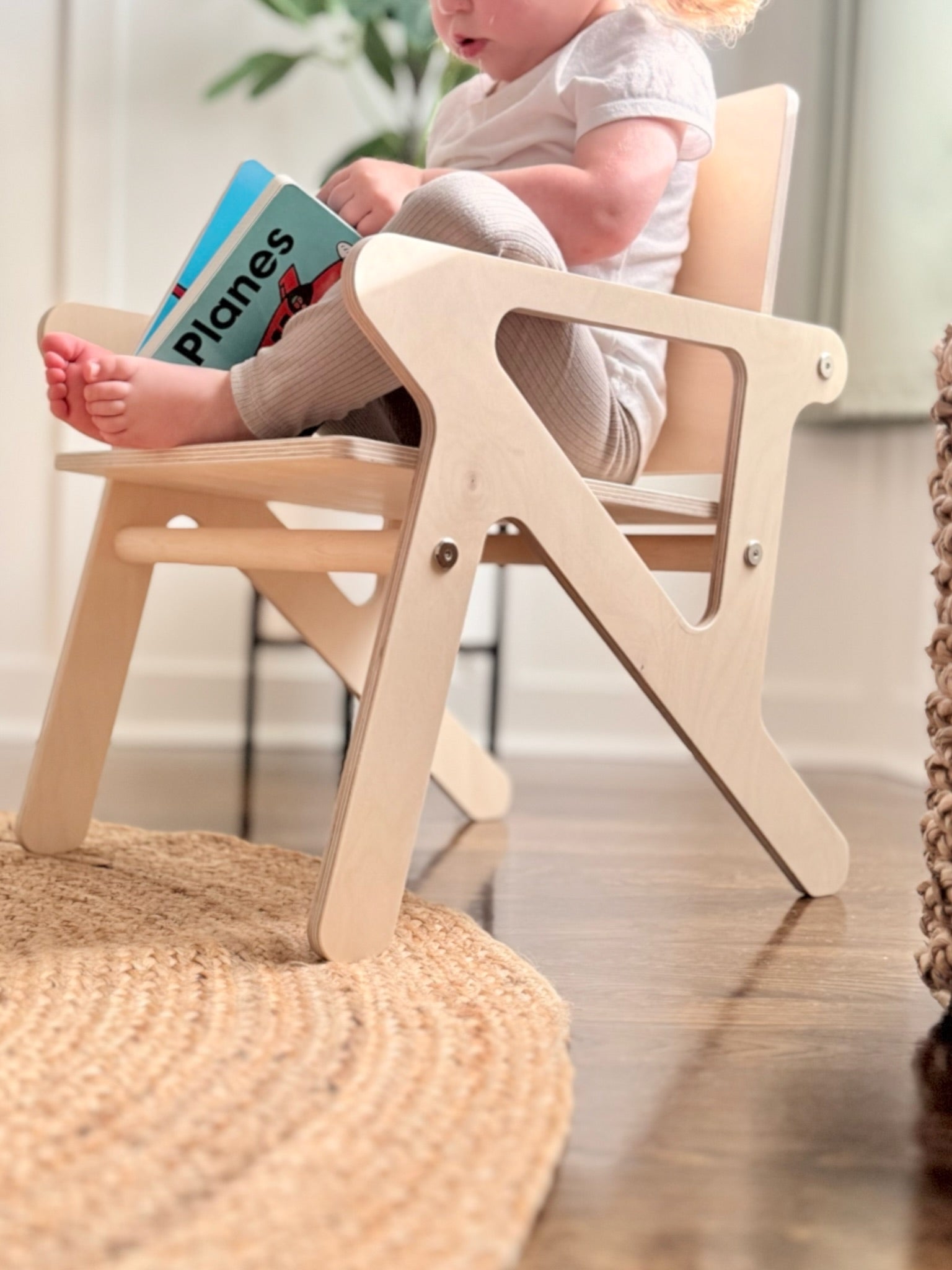 Child sitting in a wooden mid-century modern style chair holding a book indoors.