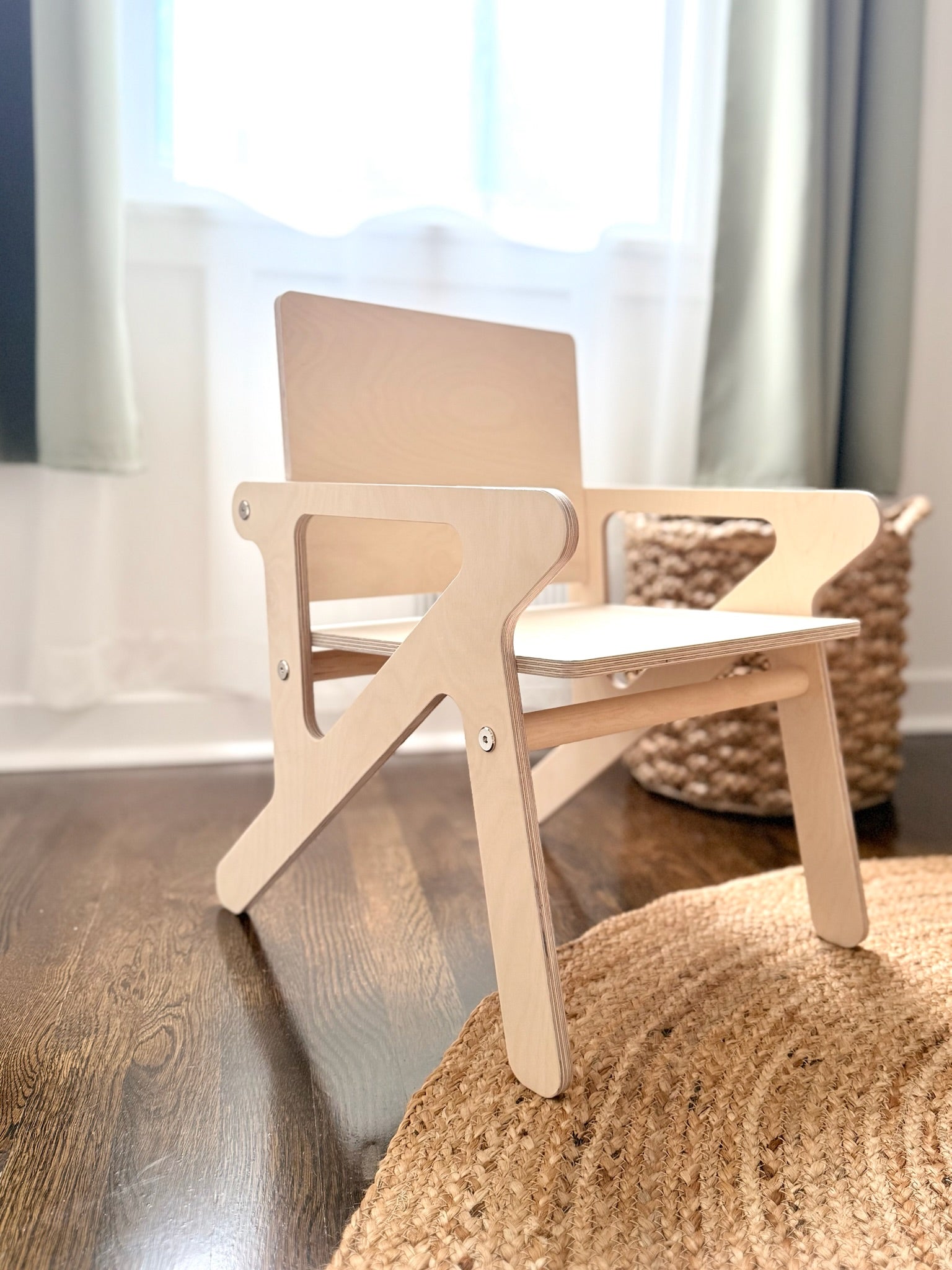 Wooden montessori mid century modern style birch children's chair on a wooden floor with curtains in the background