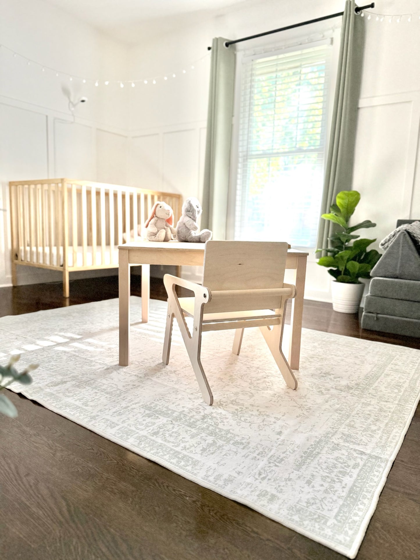 Children's room with wooden crib, table, and montessori inspired chair on a white rug.