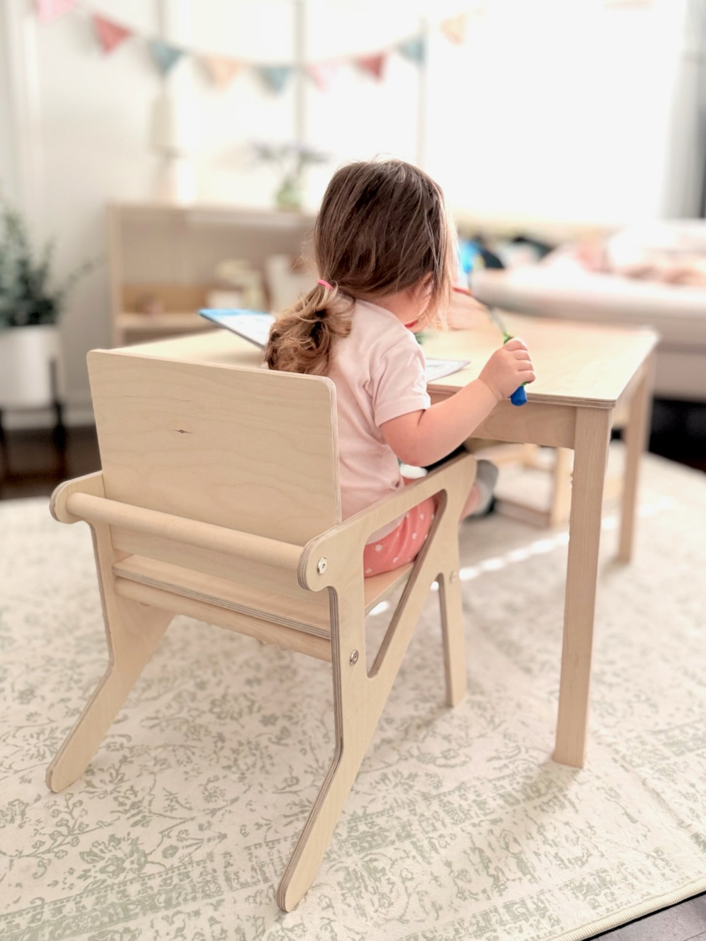 Child sitting at a montessori table with a wooden mid century modern style chair in a bright room