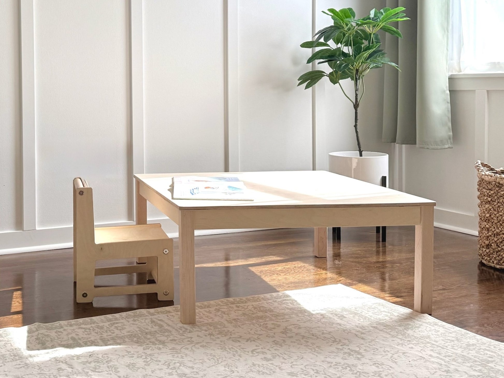 Light wooden montessori children's table with a chair in a room with a plant and rug.