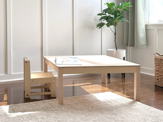Light wooden montessori children's table with a chair in a room with a plant and rug.