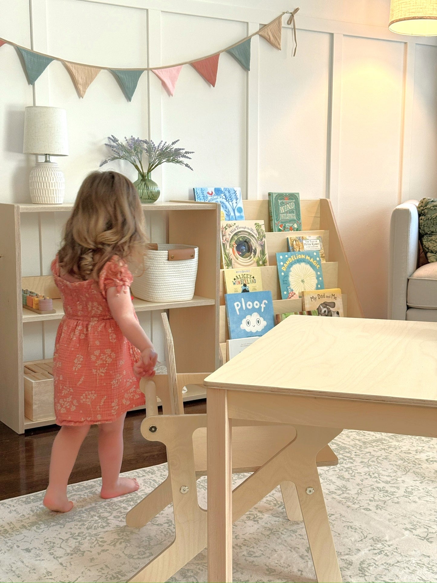Child in a playroom with books and a small wooden montessori table.