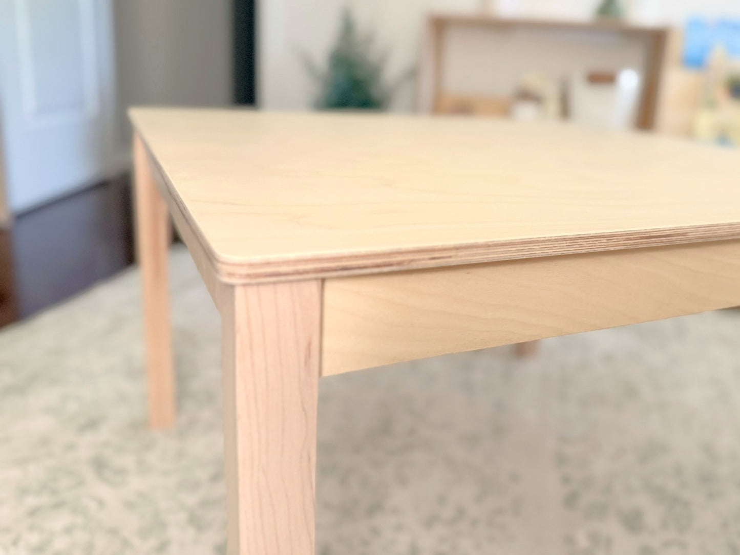 Light wooden birch childrens table with maple leg in a room with a blurred background
