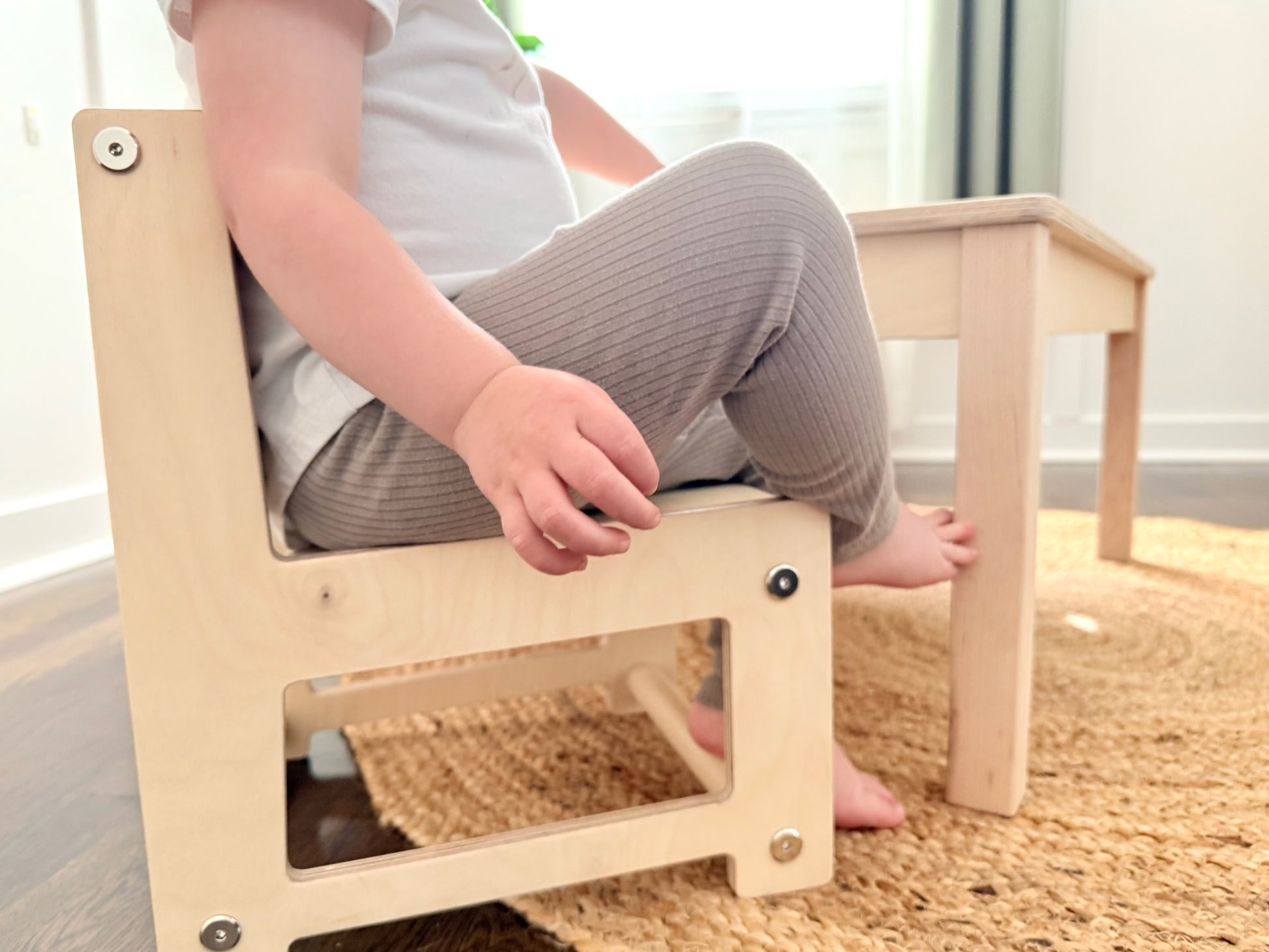 Child sitting on a small wooden montessori chair at a low table indoors.