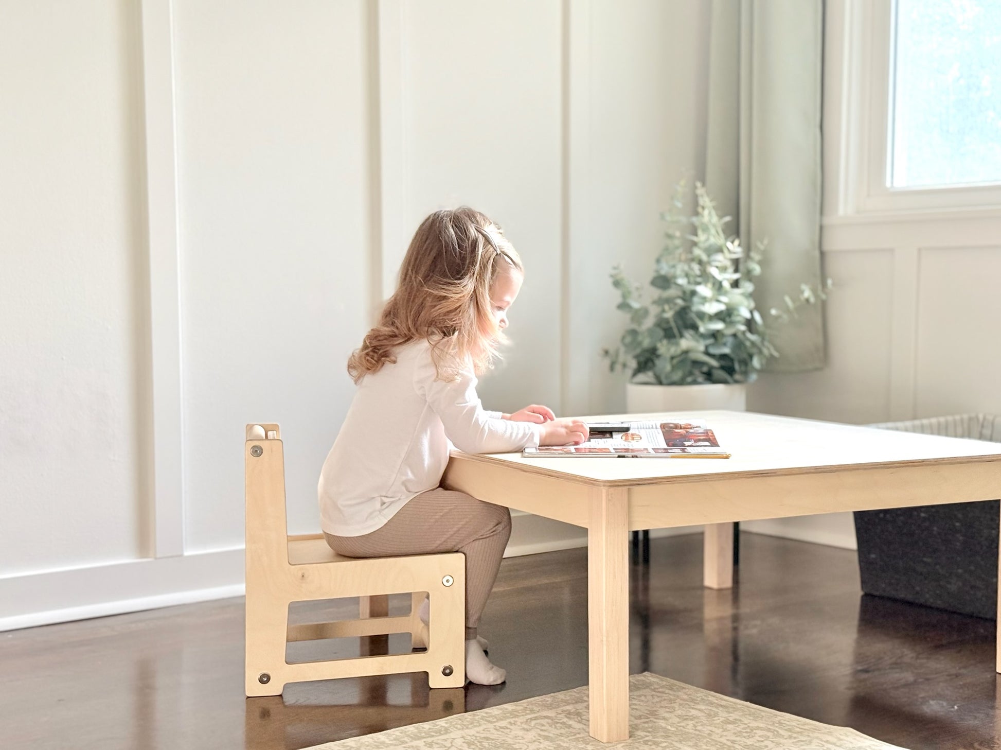 Child sitting at a small Montessori wooden table with a chair in a bright room.