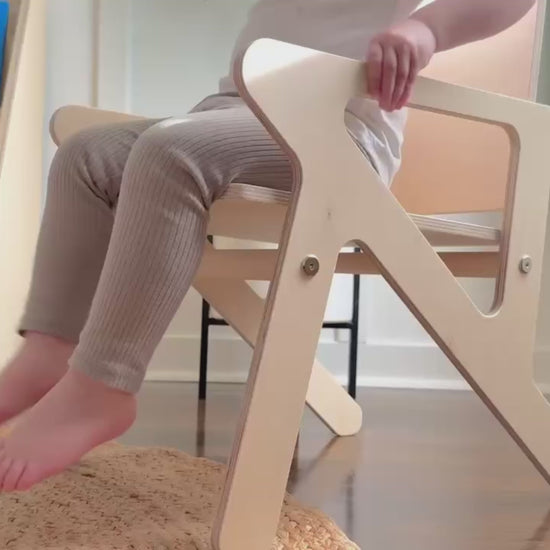 Toddler child swinging feet in a wooden mid century modern montessori style chair