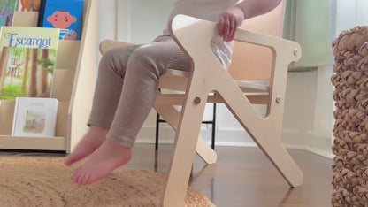 Toddler child swinging feet in a wooden mid century modern montessori style chair